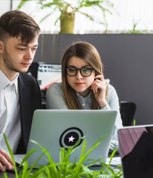 two-young-businesspeople-using-laptop-workplace_23-2147838539